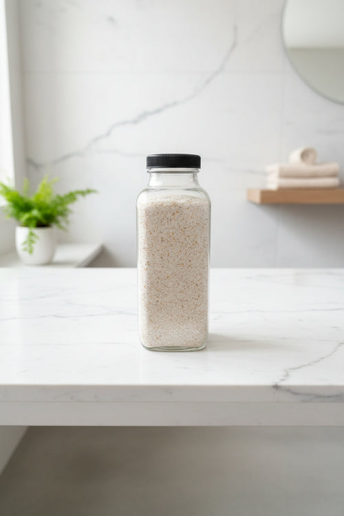 Glass bottle with black lid filled with colloidal oatmeal on a marble surface with a blurred background